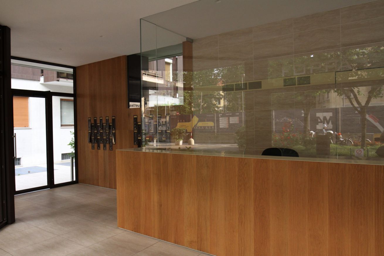 A reception area with a wooden reception desk, glass partition, and a view of the street outside.