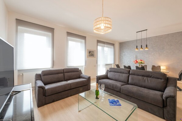 Un salon moderne avec deux canapés, une table basse en verre, un lustre et un coin repas comprenant des chaises et une table.