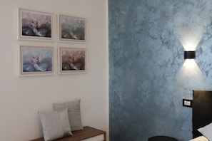 Une pièce avec un mur bleu à texture, un banc en bois avec des coussins et quatre tableaux floraux encadrés.