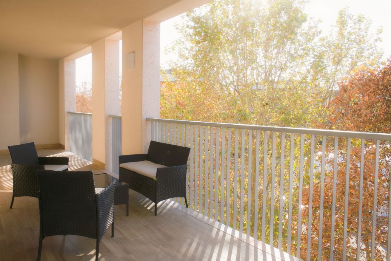 A balcony with wicker furniture, a railing, and a view of trees.