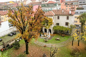 Une cour avec un arbre, des sièges en plein air et un bâtiment orné d’arches.