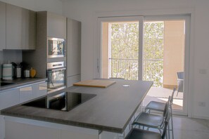 Une cuisine moderne dotée d’un grand îlot central, d’appareils électroménagers intégrés et d’une porte-fenêtre coulissante donnant sur un balcon.