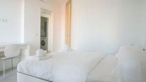 A modern hotel room with a bed, a desk, a chair, and a washing machine.