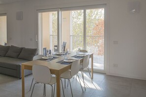 A modern living room with a dining table set for four, a grey sofa, and a large sliding glass door leading to an outdoor area. - GOVONE, 78 · Ampio e luminoso appartamento con terrazza (Milano)
