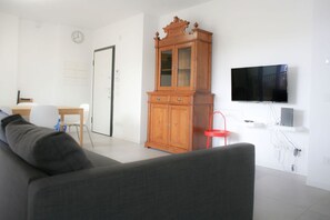 A living room with a sofa, a wooden cabinet, a television, and a dining area with chairs and a table. - GOVONE, 78 · Ampio e luminoso appartamento con terrazza (Milano)