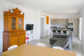Un salon moderne avec un meuble en bois, une table à manger, un canapé gris et un coin cuisine équipé de meubles et d’appareils électroménagers.
