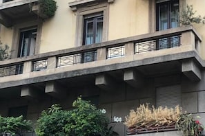 Um edifício com várias andares, varandas, janelas e algo de vegetação.