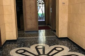 A hallway with a patterned floor, a door leading to another room, and a window with a geometric design. - Guercino, 8 – Renovated design apartment (Milano)