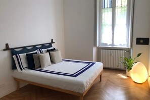 A bedroom with a bed, a window with blinds, a radiator, and a bedside lamp. - Guercino, 8 – Renovated design apartment (Milano)