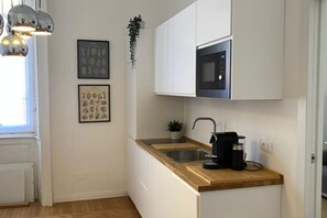 A modern kitchen with white cabinets, a wooden countertop, a built-in microwave, and a coffee machine. - Guercino, 8 – Renovated design apartment (Milano)