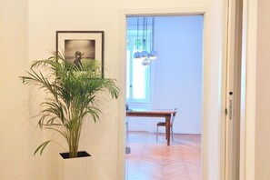 Un couloir avec une plante en pot, un tableau encadré au mur et une table à manger en bois, accompagnée de chaises.