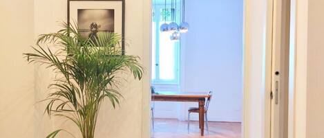 A hallway with a potted plant, a framed picture on the wall, and a wooden dining table with chairs.