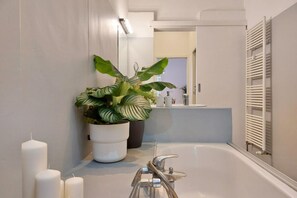 Une salle de bain avec une baignoire, une plante en pot et un miroir.
