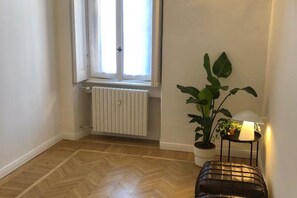 A room with a radiator, a window with curtains, a potted plant, and a lamp on a side table. - Guercino, 8 – Renovated design apartment (Milano)