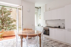 Una cuina moderna amb armaris blancs, una cuina de gas i zona de dinar amb taula de fusta i cadires transparents.