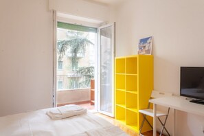 Una habitació amb un llit, una taula de treball, una televisió i un moble d'estanteries groc.