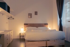 A bedroom with a bed, bedside table, hanging clothes rack, and a small framed picture on the wall.