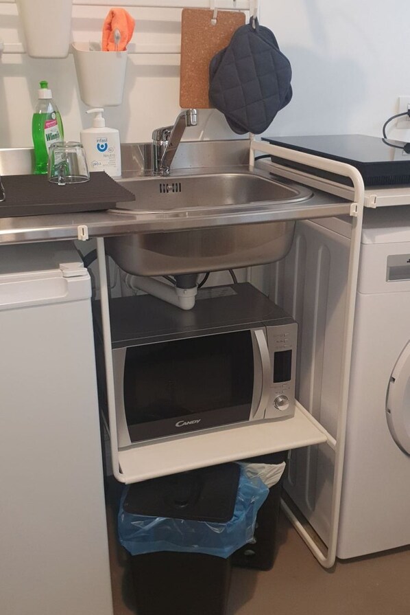 Kompakti keittiö, jossa on sisäänrakennettu mikroaaltouuni, pesuallas ja pieni roskakori.