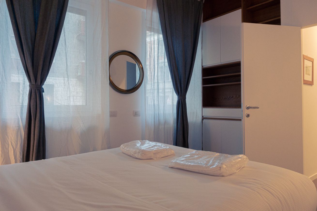 Una camera d'albergo con un letto, uno specchio, un armadio e tende leggere.