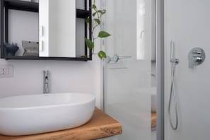 Un bany modern amb un mànec blanc, un mirall, una dutxa i una planta.