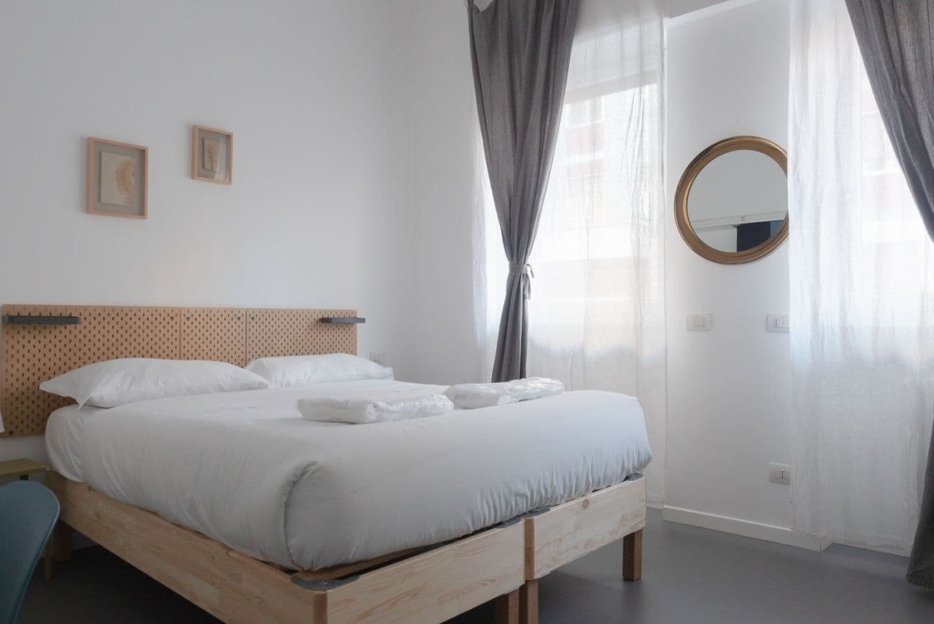 A neatly made bed with white linens, a wooden headboard, and a round mirror on the wall.