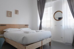 A neatly made bed with white linens, a wooden headboard, and a round mirror on the wall.