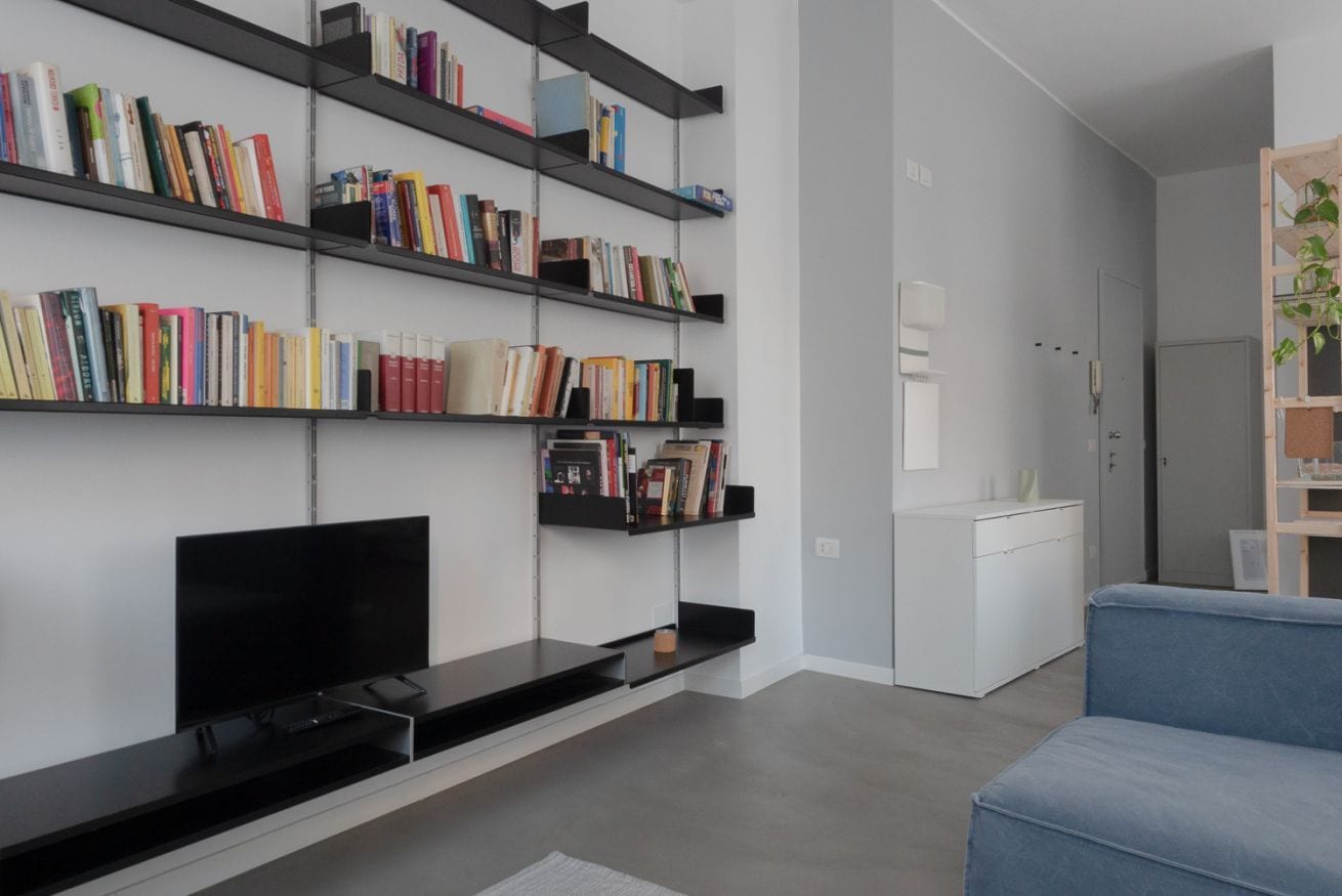 A modern living room with a flat-screen TV, a blue sofa, a bookshelf filled with books, and a white cabinet.
