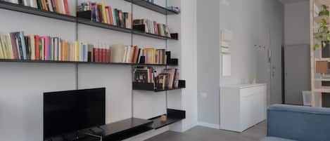 A modern living room with a flat-screen TV, a blue sofa, a bookshelf filled with books, and a white cabinet.