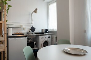 Una cucina compatta con lavatrice, forno a microonde, bollitore e un tavolo con vassoio.