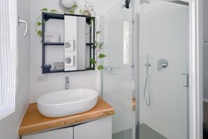 Un bagno con un lavandino bianco, uno specchio e una doccia.