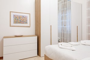 Un dormitorio con cama, una mesita de noche con un plato, un armario de madera, un cuadro en la pared y un baño con cortina.