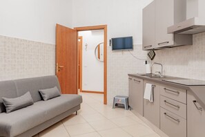 Una cocina moderna con un sofá gris, un televisor y un taburete pequeño.
