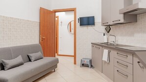 Une cuisine moderne avec un canapé gris, un téléviseur et un petit tabouret.
