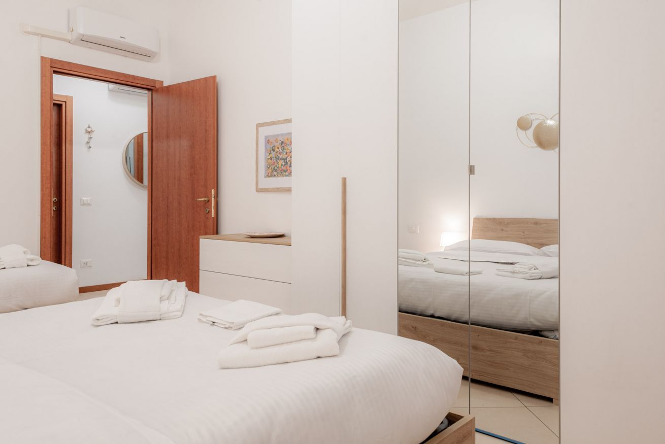 A hotel room with a bed, a wooden wardrobe, a mirror, and a small table.