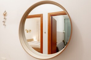 Un miroir rond avec un cadre en bois, qui reflète une chambre à coucher avec un lit, une table de chevet et un luminaire fixé au mur.