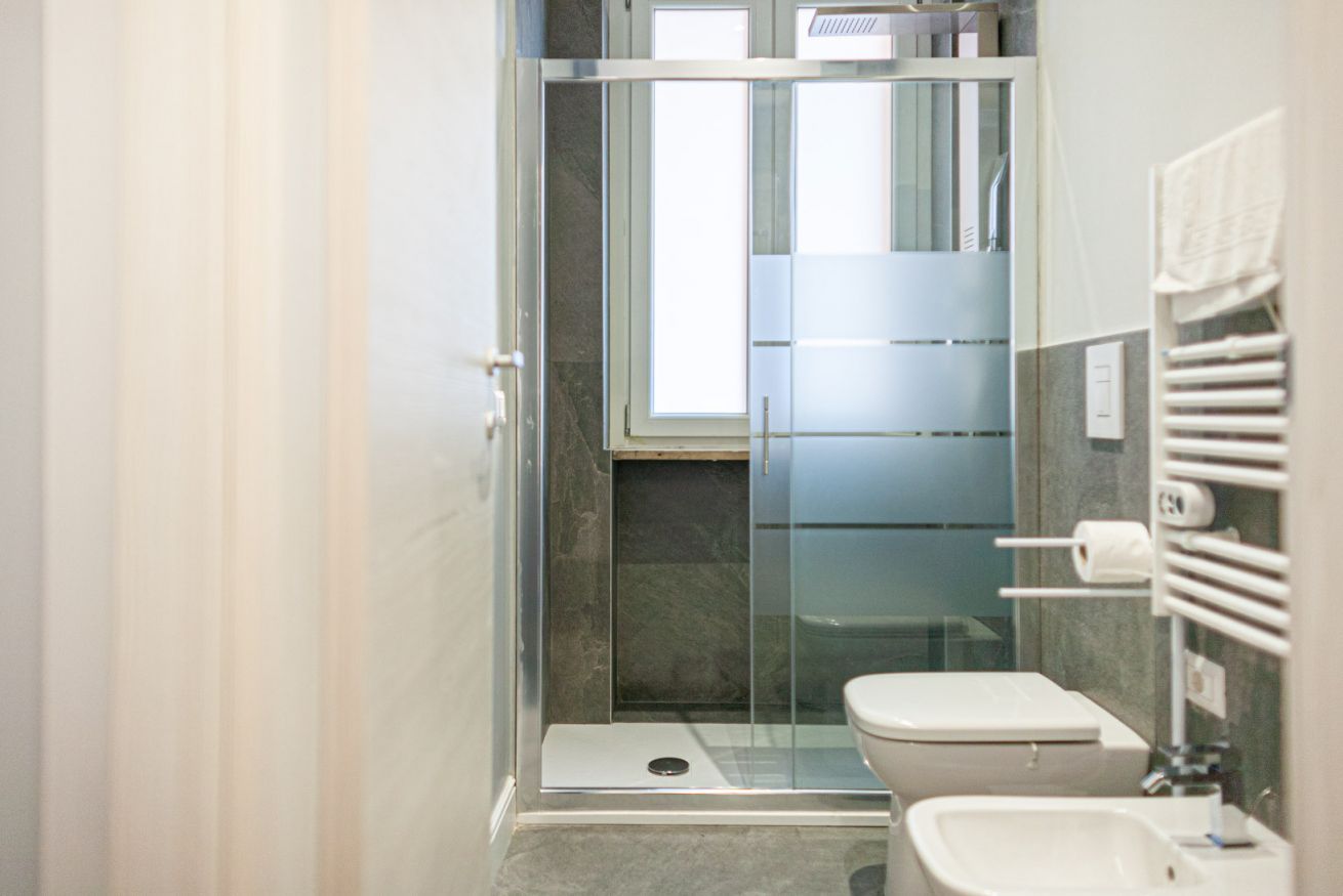 A modern bathroom with a glass-enclosed shower, a toilet, and a sink.