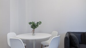 Una mesa redonda blanca con cuatro sillas blancas, una planta pequeña en un florero de vidrio y un sofá gris oscuro.