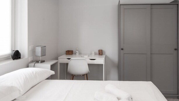 Un dormitorio con cama, escritorio, silla, armario y lámpara.