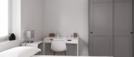 A bedroom with a bed, a desk, a chair, a wardrobe, and a lamp.