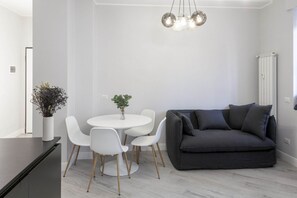 Ein modernes Wohnzimmer mit einem dunkelgrauen Sofa, weißen Sesseln, einem runden Tisch und einer Pendelleuchte.