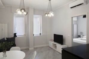 A modern hotel room with a flat-screen TV, two pendant lights, a dining table, and a bed with a nightstand. - PERGOLESI, 6 - CONSALVI · Accogliente e moderno a due passi da tutto (Milano)