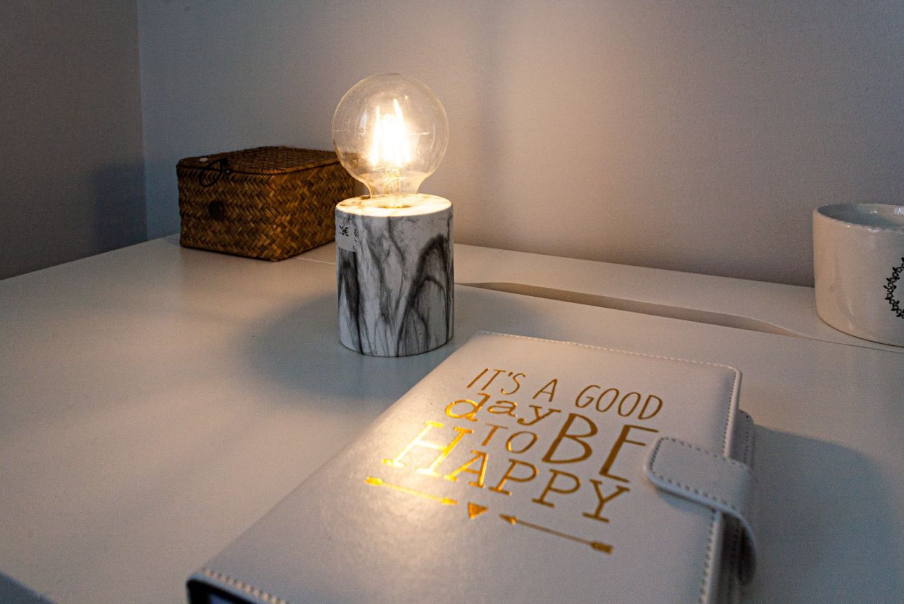 Une table avec une lampe de table allumée, une boîte décorative et un carnet contenant une citation inspirante.