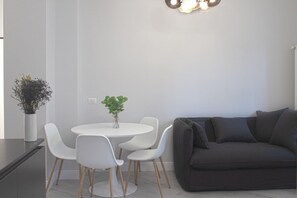 A modern living room with a round white table, four white chairs, a dark grey sofa, and two potted plants. - PERGOLESI, 6 - CONSALVI · Accogliente e moderno a due passi da tutto (Milano)