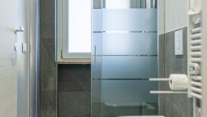 Un baño con inodoro, cabina de ducha de vidrio y barra para toallas.