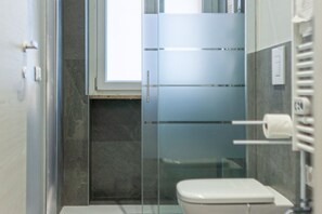 Une salle de bain équipée de toilettes, d’une douche à parois de verre et d’un porte-serviettes.