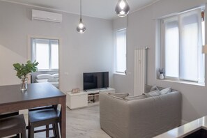 A modern living room with a sofa, TV, dining table, and chairs.