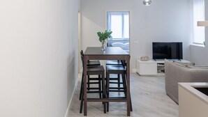 Un espacio de estar moderno con comedor, sofá, televisor y ventana que deja entrar luz natural.