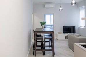 A modern living space with a dining area, a sofa, a TV, and a window with natural light.