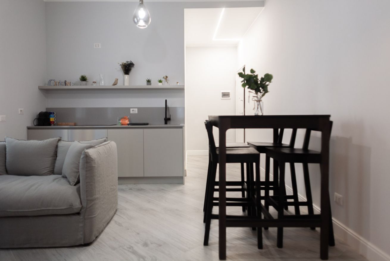 A modern kitchen with grey cabinets, a dining table with chairs, and a sofa.