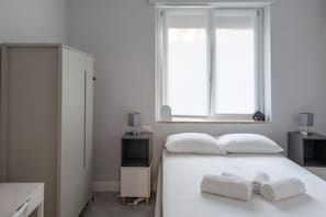 A bedroom with a bed, two bedside tables, a wardrobe, and a window with a view.